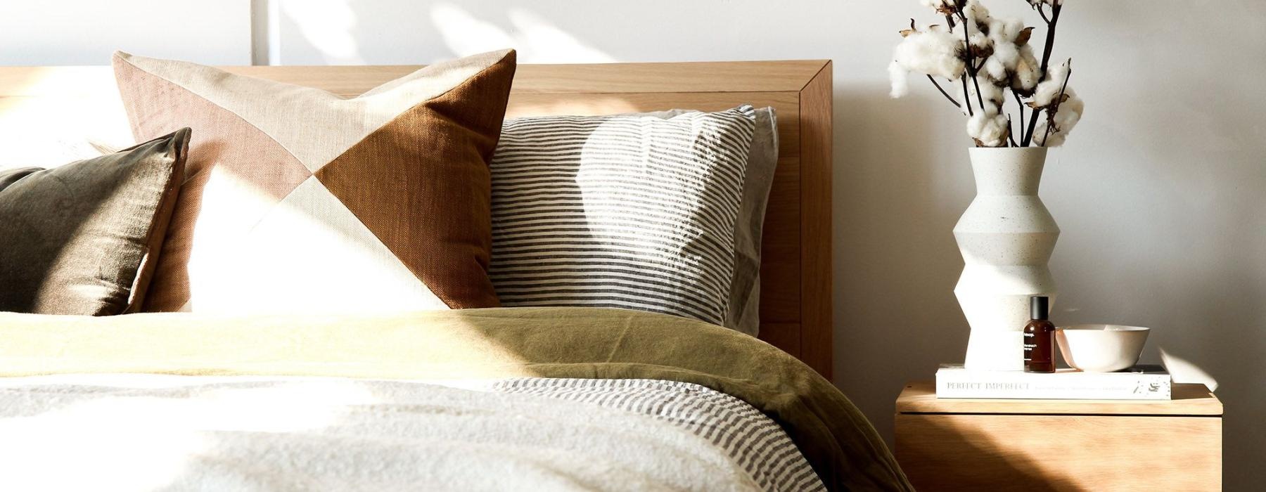 swath of sunlight shines across a well made bed and bedside table with a vase of cotton plants